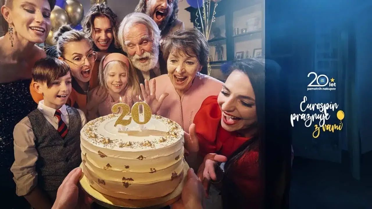 Multi-generational Slovenian family laughing around a celebration cake with a glowing gold "20" candle, alongside the Eurospin praznuje z vami 20-year anniversary lockup